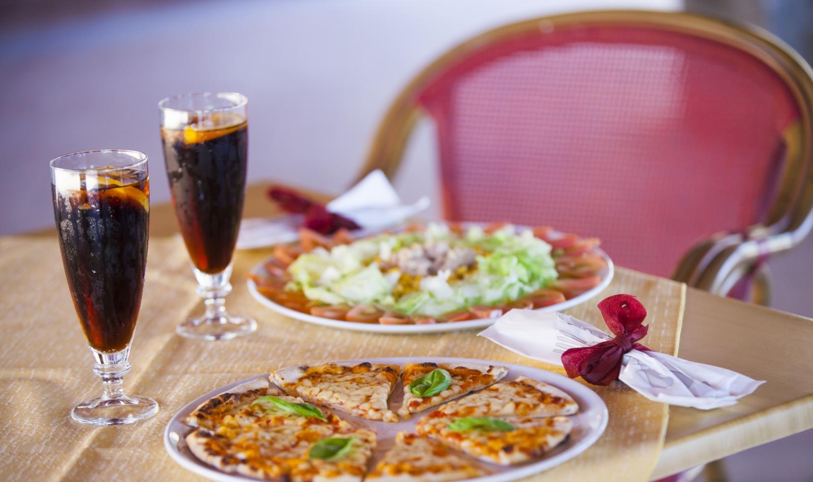 Pizza e insalata con due bicchieri di bevanda scura su un tavolo apparecchiato.