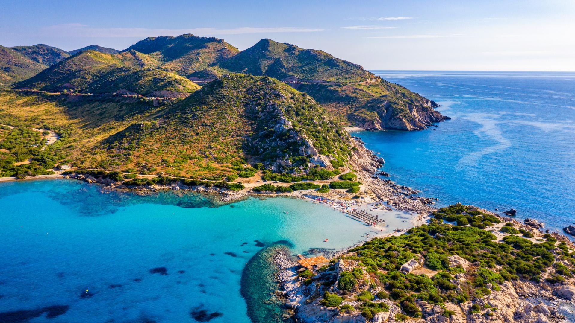 Spiaggia con acque turchesi e colline verdi in un paesaggio costiero panoramico.