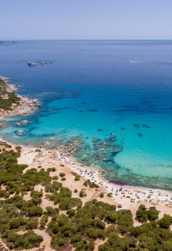 Spiaggia con mare cristallino, sabbia dorata e vegetazione mediterranea, ideale per relax estivo.